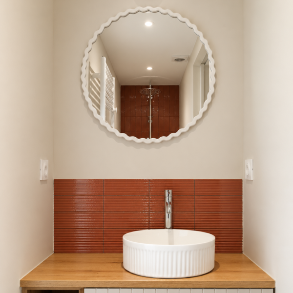 Espace vasque sur-mesure avec crédence striée terracotta, vasque ronde à cannelures et miroir rond ondulé blanc dans une salle d'eau à Valras-Plage par Sophie Pico