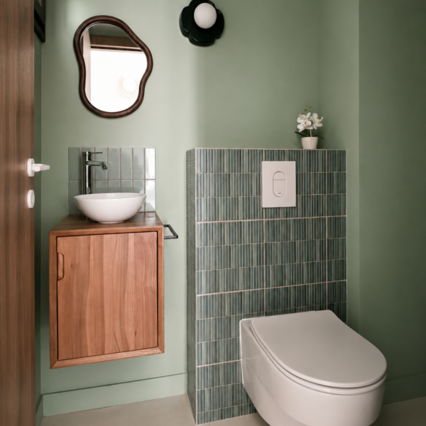Toilettes suspendues avec coffrage habillé de mosaïque kit-kat verte, lave-mains sur meuble en bois, miroir organique et murs vert sauge à Valras-Plage par Sophie Pico